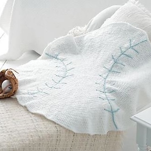 May include: White crocheted baby blanket with a blue baseball stitch design. The blanket is draped over a white chair with a white pillow.