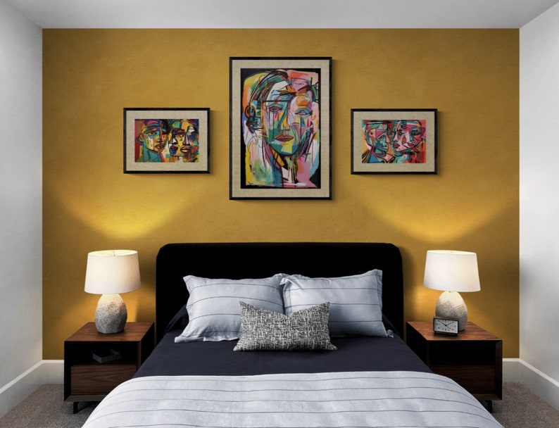 Puede incluir: Un dormitorio con una pared de color amarillo mostaza y tres pinturas abstractas de rostros. La cama tiene una cabecera negra y un edred&oacute;n a rayas azul marino y blanco. Hay dos mesitas de noche con l&aacute;mparas.