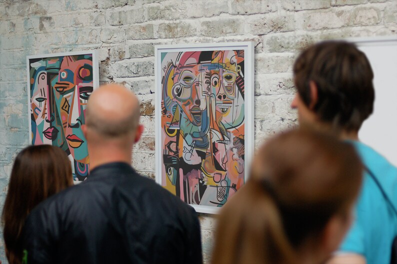 Puede incluir: Personas mirando pinturas de arte abstracto con formas geom&eacute;tricas y caras coloridas. Las pinturas est&aacute;n enmarcadas en blanco y colgadas en una pared de ladrillo blanco.