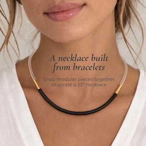Puede incluir: Un collar negro con detalles dorados y un cordón transparente y flexible. El collar mide aproximadamente 56 cm de largo. El texto de la imagen dice: "Un collar hecho de pulseras. Une piezas modulares para crear un collar de 22"."