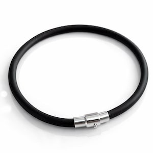 May include: A black, circular necklace with a magnetic clasp. The necklace is made of a thick, rubbery material. The clasp is silver-colored and connects the two ends of the necklace. The necklace is displayed on a white background.