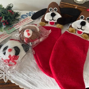 May include: Christmas-themed door knob covers and stockings. The image features two dog-shaped door knob covers, two red stockings, and two other door knob covers in packaging. The text on the packaging reads "Christmas Knobbies Door Knob Covers."