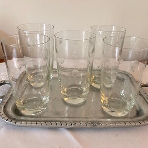 May include: A set of five clear glass tumblers featuring an etched pattern of small stars and circles, arranged on a rectangular silver-toned metal serving tray with two side handles and a decorative ridged border along the edge.