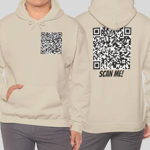 Puede incluir: Dos sudaderas con capucha beige con un código QR en blanco y negro impreso en la parte delantera y trasera. La parte trasera de una sudadera dice "SCAN ME!"