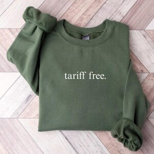 May include: An olive green sweatshirt with the text "tariff free" in white. The sweatshirt has a crew neck and long sleeves with gathered cuffs. The garment is made of a soft material.
