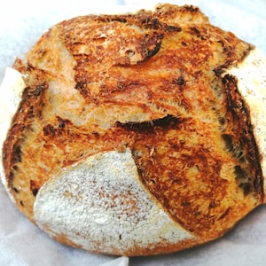 May include: A freshly baked sourdough loaf with a golden brown crust and a slightly cracked surface.