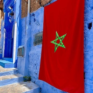 May include: A red flag with a green five-pointed star hangs on a blue wall. The star is a symbol of Morocco.