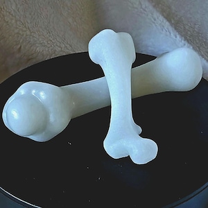 May include: Two white ceramic dog chew toys shaped like bones. The toys are on a black surface.