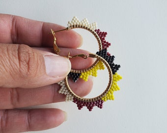 May include: A pair of gold hoop earrings with a beaded design. The beads are white, yellow, black, and red. The earrings are a statement piece and would be a great addition to any jewelry collection.