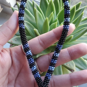 May include: A black and blue beaded lanyard with a silver key ring. The lanyard is made of small beads and has a woven pattern.
