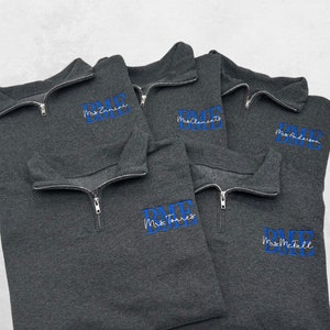 May include: Five gray quarter-zip sweatshirts with blue embroidered text that reads "BME" and the teacher's last name. The sweatshirts are stacked on top of each other.