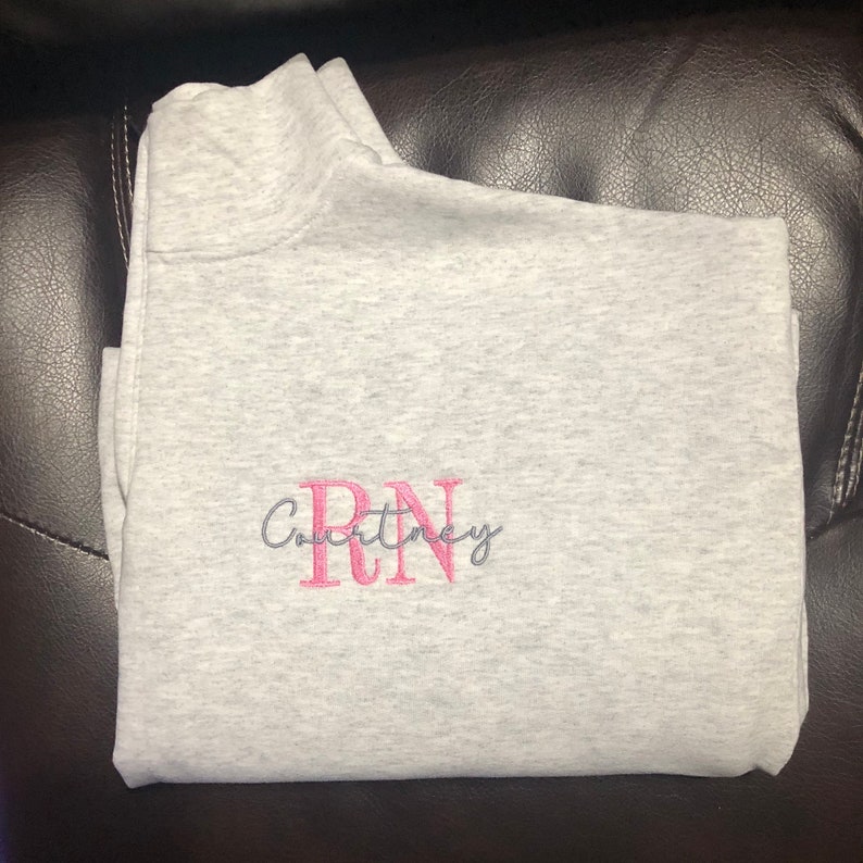 Ash gray 1/4 quarter zip sweatshirt with custom embroidery featuring RN in bubble gum pink in all caps with name Courtney in cursive font in steel gray thread.
