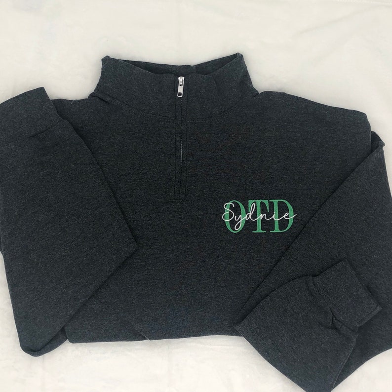 Heather black 1/4 quarter zip sweatshirt with custom embroidery featuring OTD in light green in all caps with name Sydnie in cursive font in white thread.
