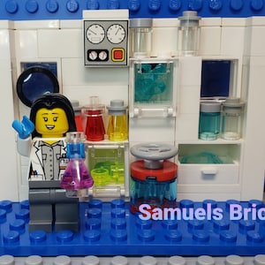 May include: A Lego minifigure of a female scientist wearing a white lab coat and holding a beaker with pink liquid. The scientist is standing in front of a white Lego lab set with various lab equipment, including beakers, test tubes, and a control panel. The set is on a blue Lego baseplate with the text "Samuels Bricks".