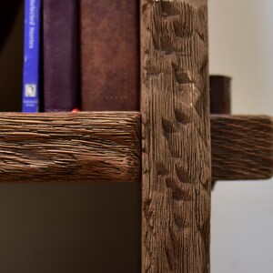 May include: Close-up of a rustic wooden bookshelf with visible grain and carved details. The shelf holds several books with varying colors and sizes, creating a warm, inviting aesthetic. The wood has a rich, brown tone.