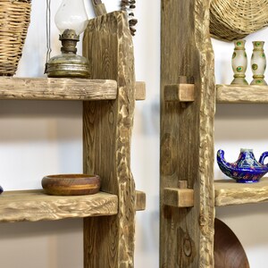May include: Rustic wooden shelves with a natural, unfinished look. The shelves are supported by vertical wooden beams with visible joinery. Various decorative items are displayed, including a vintage oil lamp, a wooden bowl, and a blue genie lamp.