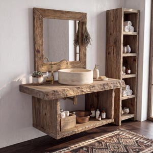 May include: A rustic bathroom vanity set featuring a live-edge wooden countertop, a round stone vessel sink, and a matching wooden mirror frame. The unit includes a tall open shelving tower, a brass faucet, and various bathroom accessories.