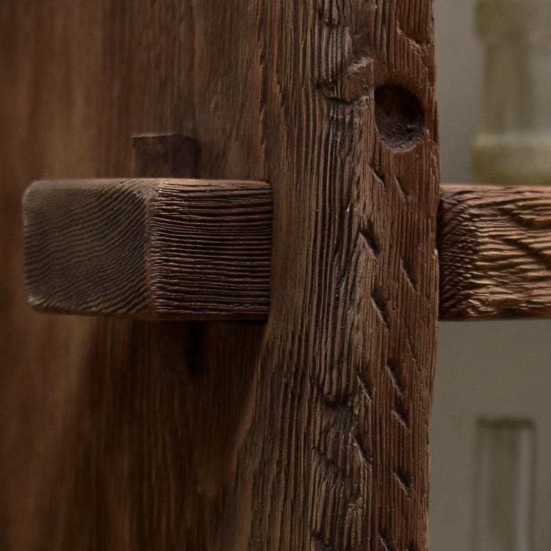May include: Close-up of a rustic wooden latch and frame, showcasing the natural grain and texture of the aged wood. The latch is rectangular and projects from the frame, secured by a small wooden peg. The wood is a warm brown color.
