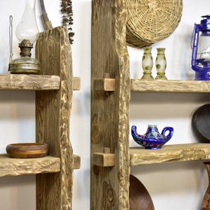May include: Rustic wooden shelves with a natural, unfinished look. The shelves are adorned with various decorative items, including a vintage oil lamp, a wooden bowl, and a blue and gold genie lamp. A woven basket and a blue lantern are also visible.