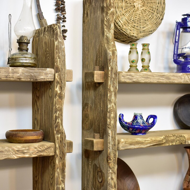 May include: Rustic wooden shelves with a natural, unfinished look. The shelves are adorned with various decorative items, including a vintage oil lamp, a wooden bowl, and a blue and gold genie lamp. A woven basket and a blue lantern are also visible.