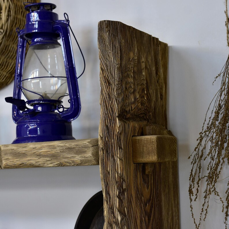 May include: A rustic display featuring a vibrant blue lantern with a glass globe, set on a weathered wooden shelf. A large, textured wooden beam stands beside it, creating a warm, inviting atmosphere. The scene evokes a vintage, farmhouse aesthetic.