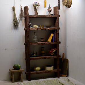 May include: A rustic, wooden bookshelf with multiple shelves, displaying various decorative items. The shelves hold books, vases, and small ornaments. A small wooden stool with a green melon sits in front of the bookshelf.