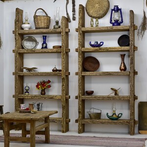 May include: Two rustic wooden shelves filled with decorative items. The shelves hold a variety of objects, including lanterns, vases, baskets, and small dishes. A small wooden table is in front of the shelves, with a tray of items on top.