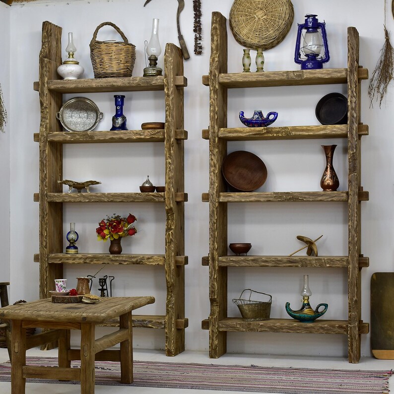 May include: Two rustic wooden shelves filled with decorative items. The shelves hold a variety of objects, including lanterns, vases, baskets, and small dishes. A small wooden table is in front of the shelves, with a tray of items on top.
