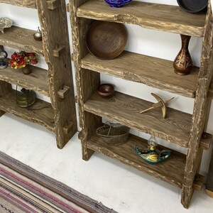 May include: Two rustic wooden shelves with multiple shelves. The shelves are made of rough-hewn wood and are filled with decorative items, including bowls, vases, and small trinkets. The shelves are a natural wood color.