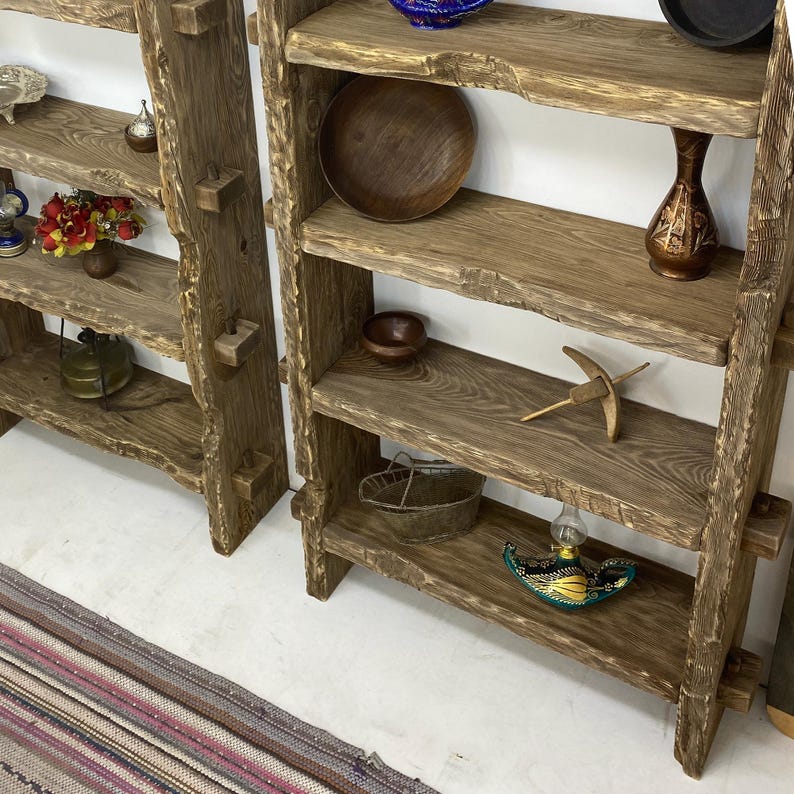 May include: Two rustic wooden shelves with multiple shelves. The shelves are made of rough-hewn wood and are filled with decorative items, including bowls, vases, and small trinkets. The shelves are a natural wood color.