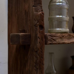 May include: Close-up of a rustic wooden shelf with a dark brown finish. The shelf features a mortise and tenon joint, showcasing the craftsmanship. A clear glass jar sits on the shelf, adding a touch of vintage charm. The wood grain is visible.