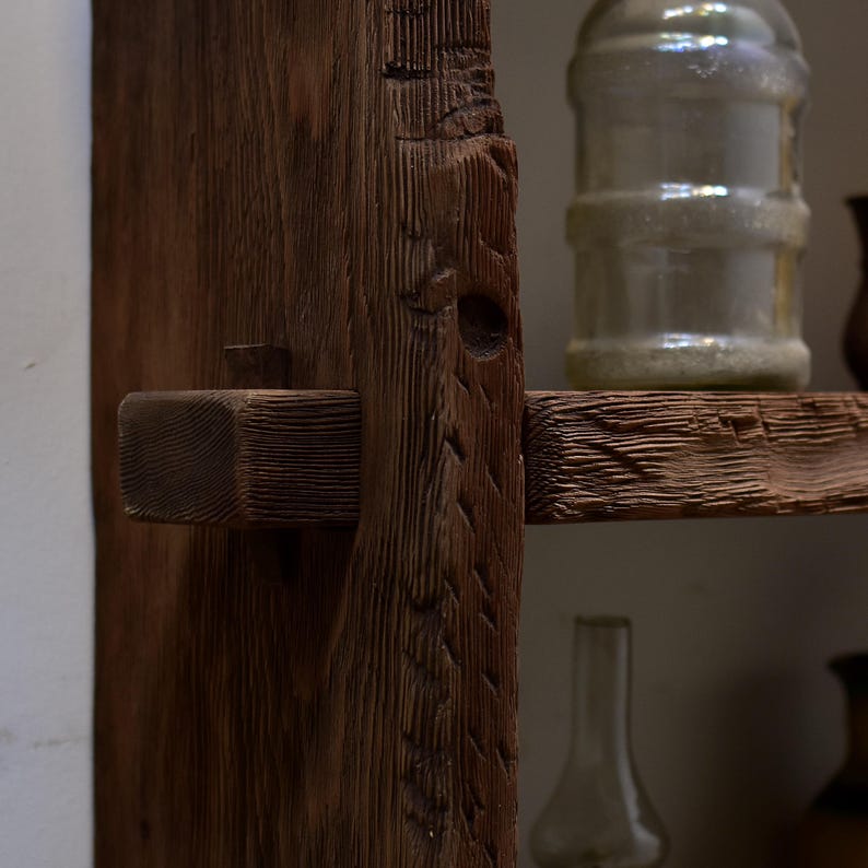 May include: Close-up of a rustic wooden shelf with a dark brown finish. The shelf features a mortise and tenon joint, showcasing the craftsmanship. A clear glass jar sits on the shelf, adding a touch of vintage charm. The wood grain is visible.