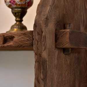 May include: Close-up of a rustic wooden shelf and support structure. The wood has a rich, dark brown color with visible grain and texture. A decorative lamp with a colorful mosaic glass shade sits on the shelf, adding a touch of elegance.