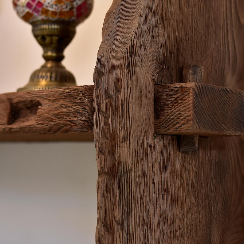 May include: Close-up of a rustic wooden shelf and support structure. The wood has a rich, dark brown color with visible grain and texture. A decorative lamp with a colorful mosaic glass shade sits on the shelf, adding a touch of elegance.
