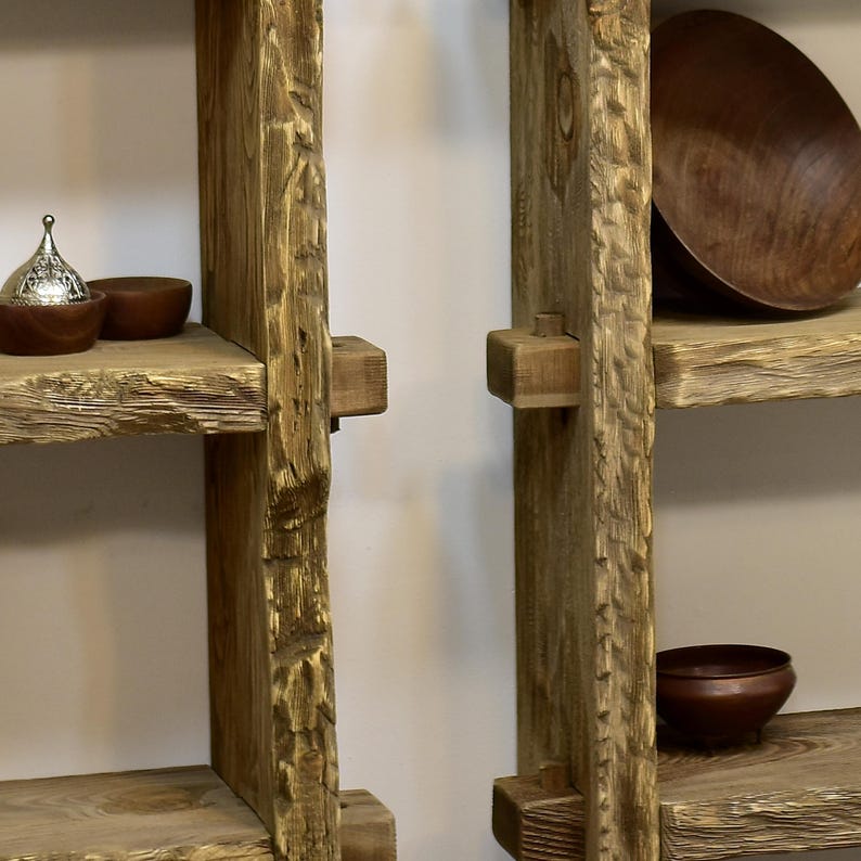 May include: Rustic wooden shelves with a natural, unfinished appearance. The shelves are constructed from thick, textured planks and feature a warm, earthy tone. Decorative bowls and a small metal container with a lid are displayed on the shelves, adding a touch of elegance.