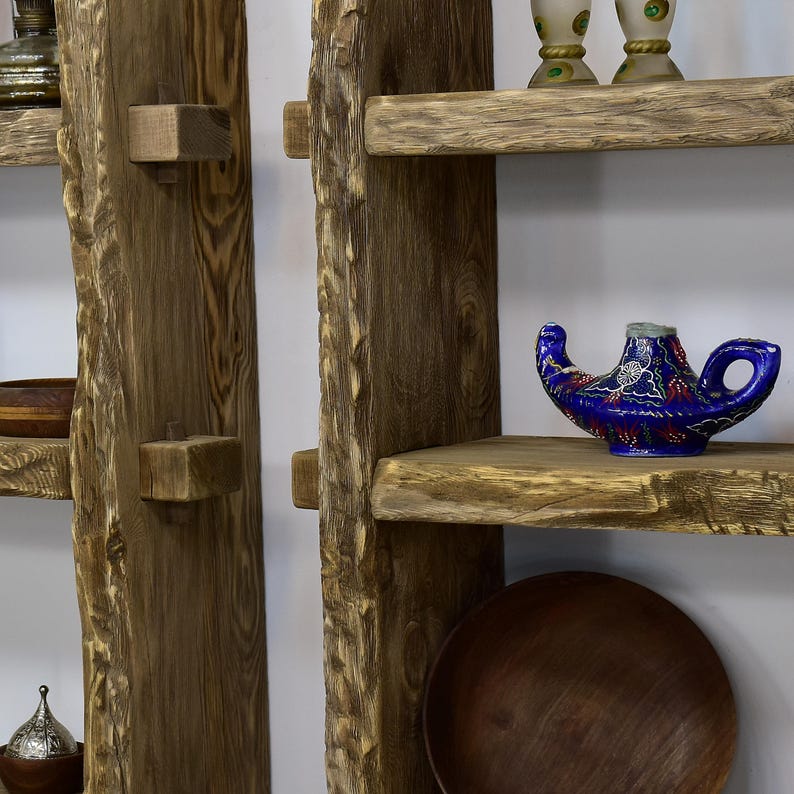 May include: Rustic wooden shelves with a natural edge design. A blue genie lamp with intricate patterns sits on one shelf. The shelves are made of light brown wood and are mounted on a white wall. A wooden bowl and decorative items are also visible.