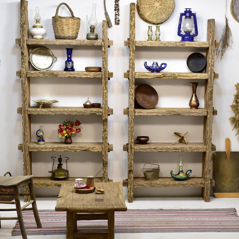 May include: Two rustic wooden shelves filled with decorative items. The shelves are made of rough-hewn wood and hold various objects, including oil lamps, vases, bowls, and baskets. A small wooden table and a rug are in front of the shelves.