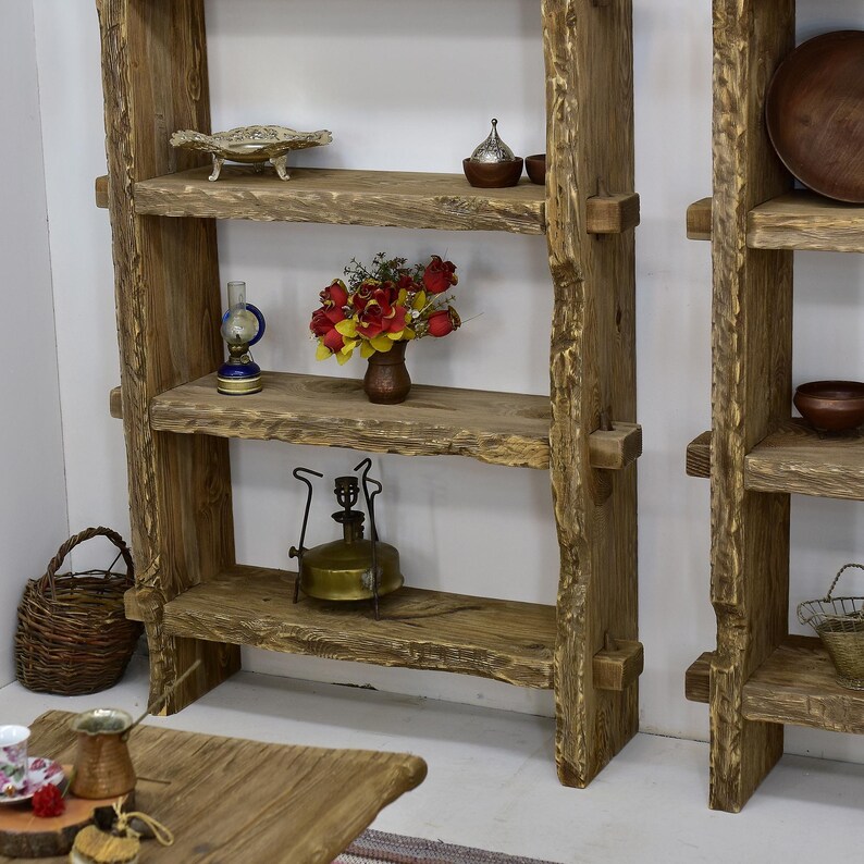 May include: Rustic wooden shelves with decorative items. The shelves are made of rough-hewn wood and hold a variety of items, including a metal bowl, a small vase of flowers, a vintage oil lamp, and a woven basket.