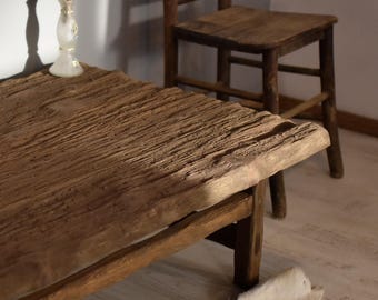 May include: A rustic wooden coffee table with a thick, weathered top and a simple, sturdy frame. The table has a natural, brown finish and is made from reclaimed wood.
