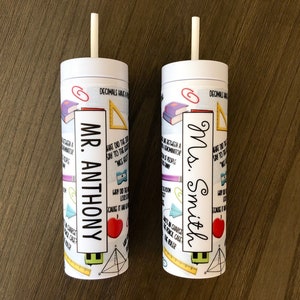 May include: Two white tumblers with straws, each featuring a different teacher's name and a variety of school-themed illustrations. The tumbler on the left says "Mr. Anthony" and the tumbler on the right says "Mrs. Smith".