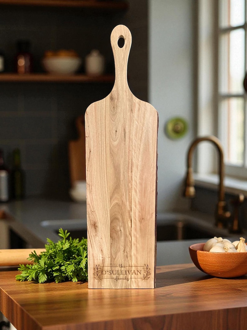 May include: A light-colored wooden cutting board with a handle and a hole for hanging. The board has the text "the O'Sullivan family" engraved on it. The board is rectangular with a natural edge.