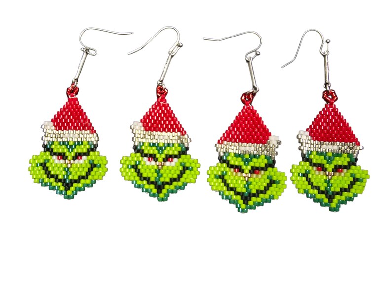 Puede incluir: Cuatro pares de pendientes novedosos con una cara verde con un gorro de Pap&aacute; Noel rojo. Los pendientes est&aacute;n hechos de peque&ntilde;as cuentas y tienen ganchos plateados. La cara tiene una expresi&oacute;n gru&ntilde;ona.
