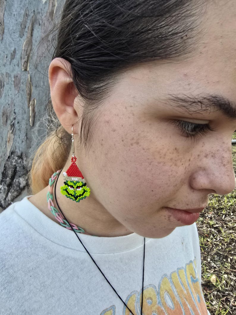 Puede incluir: Pendientes hechos a mano con cuentas que representan la cara del Grinch. Los pendientes tienen una cara verde, un gorro de Pap&aacute; Noel rojo y ganchos plateados. Un accesorio festivo para la temporada navide&ntilde;a.