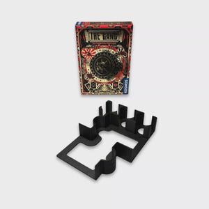 Può includere: Una scatola di gioco da tavolo intitolata "THE GANG" con un design decorativo con una porta di cassaforte, cuori e stelle. Sotto c'è un porta pezzi di gioco in plastica nera. La scatola è rossa, nera e bianca.