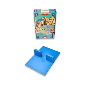 May include: A boxed card game titled "FLIP 7" with a teal, red, and yellow design. Below it is a blue game board with two raised blue sections. The game box has text in multiple languages.