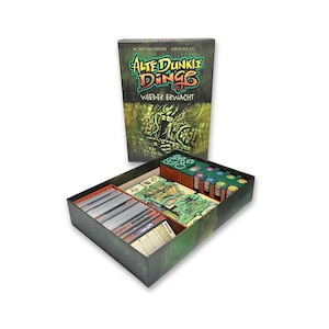 May include: A board game box and its contents are displayed. The box is dark with green and yellow accents, and the title "ALTE DUNKE DINGE" is visible. Inside, the game components are organised in a tray, including cards, tokens, and game boards.