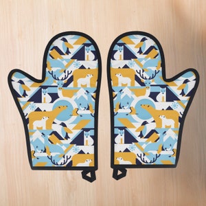 Puede incluir: Un par de guantes de horno azules y amarillos con estampado de animales de invierno. Los guantes presentan pingüinos, osos polares, zorros árticos y renos.