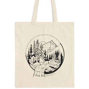 May include: A natural canvas tote bag featuring a black and white illustration of a mountain landscape with trees, a river, and the sun. Text includes "You are the light of the world" and "Matthew 5:14".
