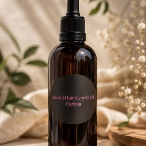 May include: A dark amber glass bottle with a black dropper cap and a round black label. The label features the text Natural Hair Growth Oil and the name Carissa in pink lettering. The bottle is cylindrical with a smooth, reflective surface.