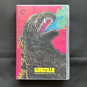 May include: A Blu-ray case for The Criterion Collection Godzilla: The Showa-Era Films, 1954-1975. The cover features a black illustration of Godzilla with a pink and yellow background, including a yellow lightning bolt and the text Godzilla.